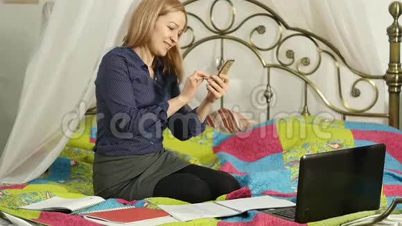 家庭在线教育与工作簿和笔记本电脑美丽的女人用她的智能手机和同学视频聊天视频的预览图