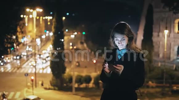 年轻漂亮的女人站在意大利罗马竞技场附近的市中心使用智能手机视频的预览图