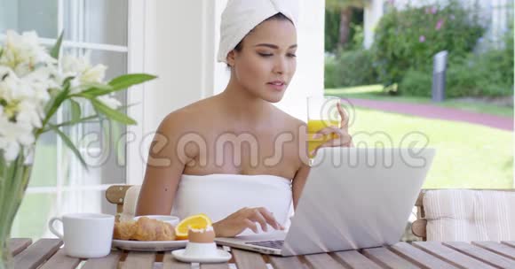 年轻女性在吃早餐时使用笔记本电脑视频的预览图