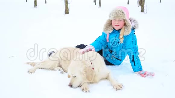 对宠物的爱女孩正和一只金色的猎犬在公园的雪地里休息视频的预览图