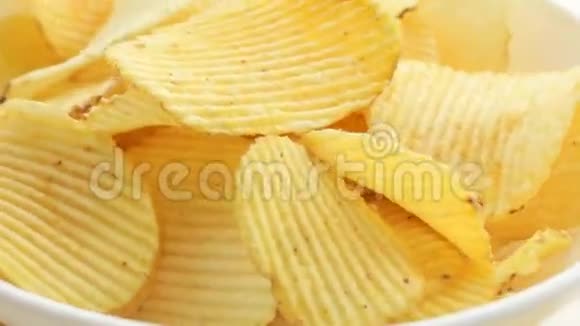 旋转不健康的有害食物黄色美味的土豆肋脆薯片随机躺在白色的桌子背景上特写视频的预览图