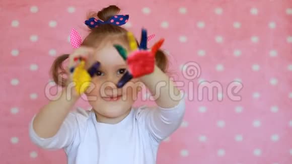 快乐的小女孩用彩绘的手有趣的孩子用手掌在五颜六色的油漆视频的预览图