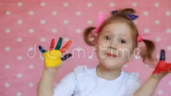 有趣的孩子用手掌在五颜六色的油漆快乐的小女孩画着肮脏的手视频的预览图