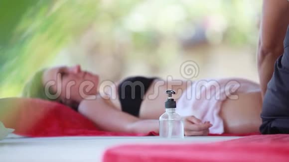 年轻女子躺在热带海滩上放松的水疗沙龙里按摩治疗师做腿油按摩1920x1080视频的预览图