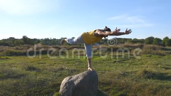 年轻的运动男子站在石头瑜伽姿势户外瑜伽在大自然中练习瑜伽动作和姿势运动员视频的预览图