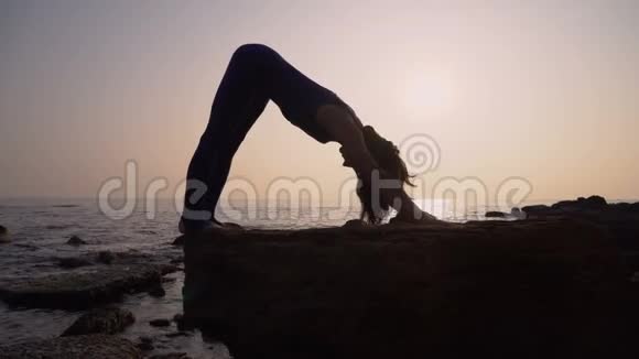 穿着紧身衣的年轻女子在令人惊叹的日出时在海面上的海滩上练习瑜伽健身运动瑜伽和健康视频的预览图