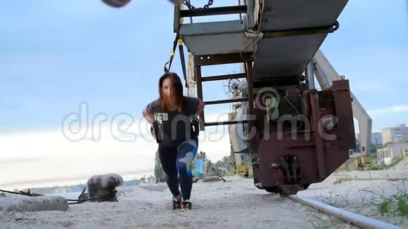 美丽的女士在悬吊带TRX的帮助下锻炼她的肌肉黎明时分在沙地上的一个货鹤附近视频的预览图