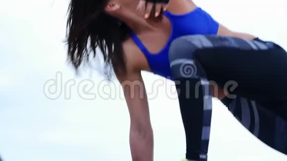 一位年轻的运动女性穿着蓝色上衣和条纹腿做力量练习户外健身视频的预览图