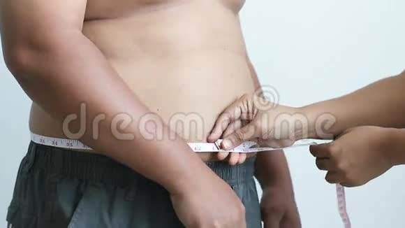 女人的双手紧贴着胖男人的腰围用卷尺视频的预览图