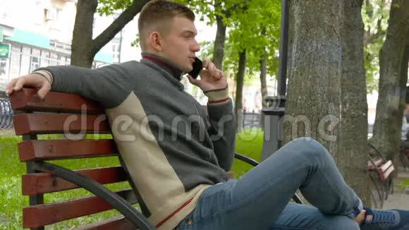 一个年轻人坐在城市公园的长椅上打电话视频的预览图