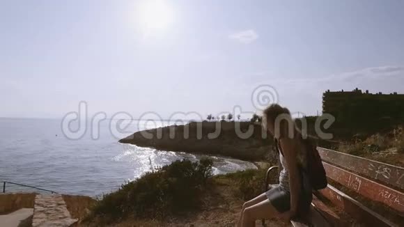 戴着太阳镜在海边的长凳上放松的漂亮快乐的女人视频的预览图