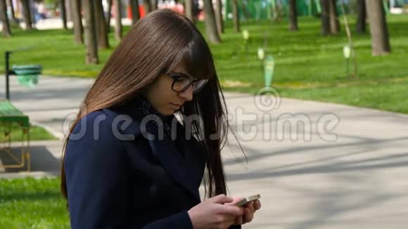 戴眼镜的漂亮女人在公园户外使用手机细节年轻迷人的快乐女孩放松视频的预览图