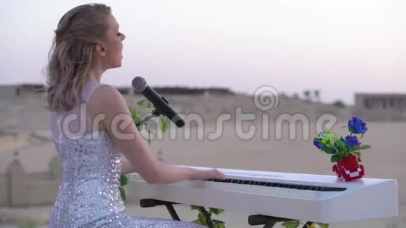优雅的年轻金发女子唱歌在大型竞技场或圆形剧场的白色数字钢琴上演奏浪漫的音乐女孩视频的预览图