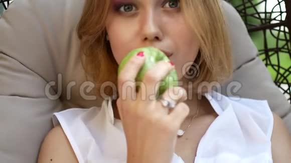 一个穿着白色连衣裙的女孩正在吃一个绿色的苹果视频的预览图