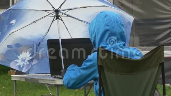 一位穿防水衣服的年轻女子在雨中用笔记本电脑工作视频的预览图
