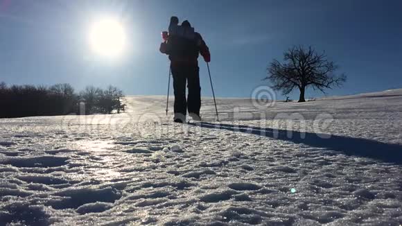 穿着雪鞋在冬天的风景中行走的人的剪影带着徒步旅行杆蓝天和视频的预览图