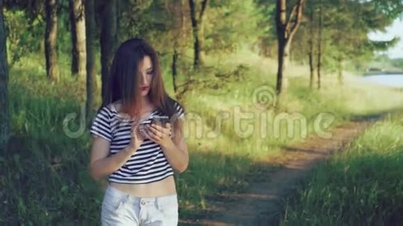 年轻女孩在外面的绿树自然背景下使用智能手机4k视频的预览图