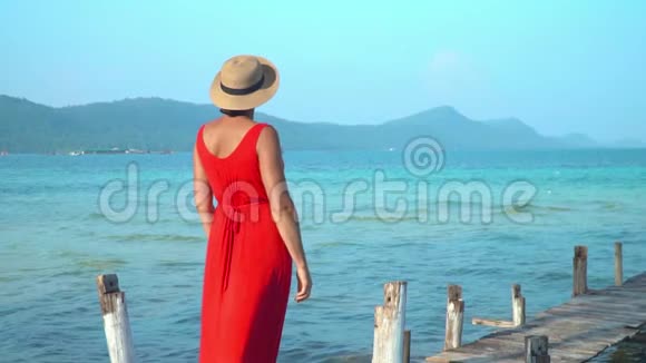穿着红色长裙的女人那个穿着红色裙子的年轻女子站在码头上远远地看着戴帽子的女人视频的预览图