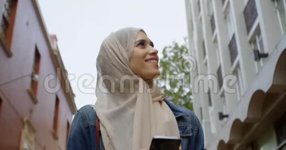戴头巾的妇女在街上行走时使用手机视频的预览图