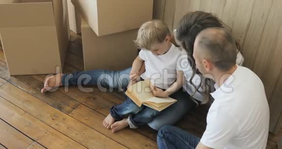 幸福而疲惫的一家人坐在他们新家的地板上家庭在打开纸箱后放松和欢笑视频的预览图
