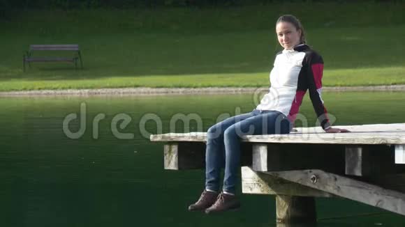 年轻女子坐在码头上摆动双腿视频的预览图