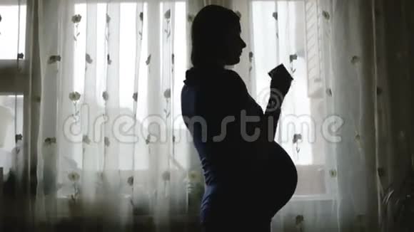一个肚子大的孕妇正在喝茶看着窗外视频的预览图