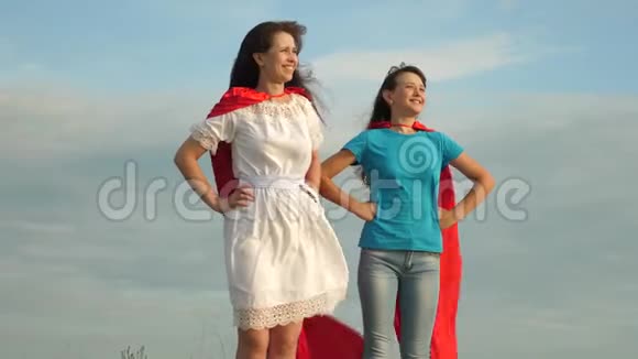 妈妈和女儿扮演超级英雄两个穿着超级英雄红色斗篷的女孩站在蓝天上风吹起了一阵视频的预览图