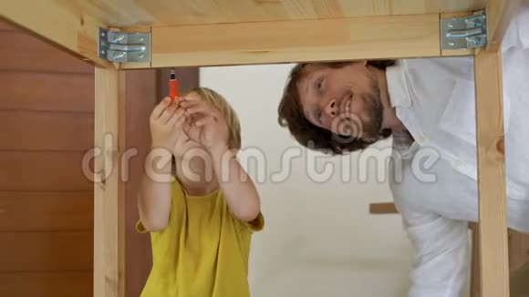父子俩用小零件组装木制家具小男孩帮助他父亲组装一张桌子视频的预览图