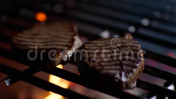 把牛排放在餐厅烤架上烧着火焰厨师把它们翻过来慢动作视频的预览图