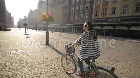 美丽的年轻女孩骑自行车在旧城阳光户外视频的预览图