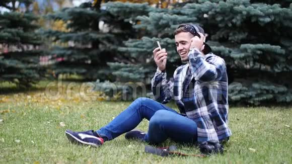 戴着耳机坐在草地上听音乐的男青年视频的预览图