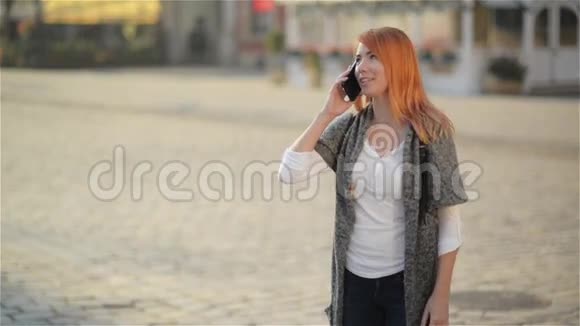 年轻的快乐兴奋的笑着女人在手机上说话红发女孩在城市的街头挥手视频的预览图