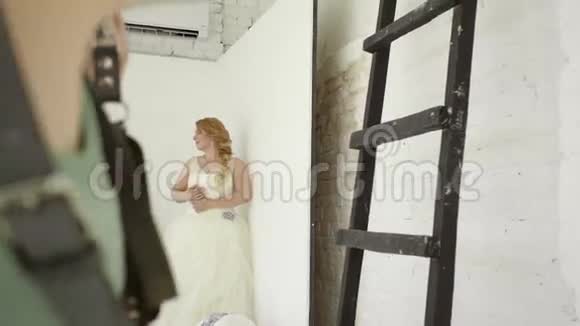 可爱的年轻金发女郎穿着婚纱在摄影棚为摄影师摆姿势视频的预览图