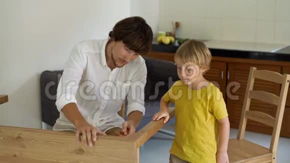 父子俩用小零件组装木制家具小男孩帮助他父亲组装一张桌子视频的预览图