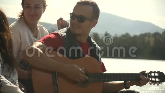 三个朋友在河岸上休息唱歌弹吉他视频的预览图