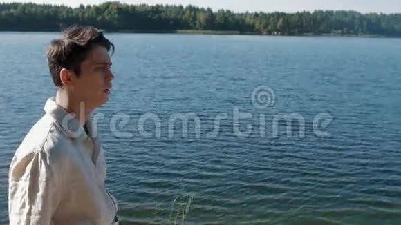 阳光明媚的夏日穿着白色衬衫的媚兰男孩在湖边散步视频的预览图