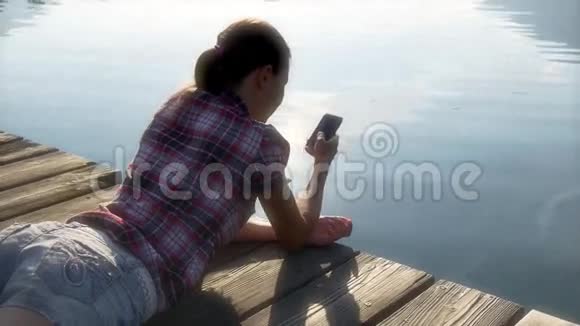智能手机上的女孩短信躺在木制码头上视频的预览图