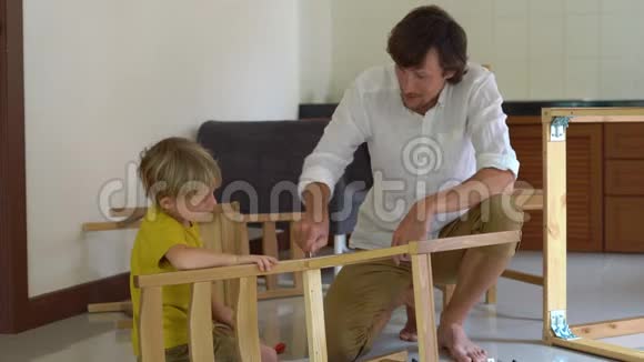 父子俩用小零件组装木制家具小男孩帮助他父亲组装一把椅子视频的预览图