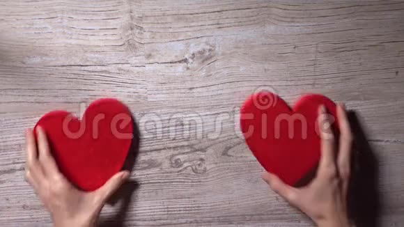 年轻女子把两颗红心放在木桌上俯视浪漫爱情情人节关系概念视频的预览图