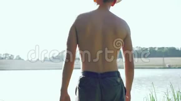 戴着太阳镜和帽子的男孩的背影来到池塘伸展双手4k视频的预览图
