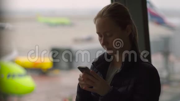 一名年轻女子在机场的一扇大窗户前用智能手机慢镜头视频的预览图