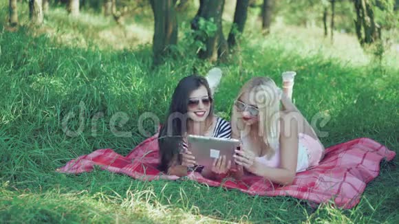 快乐的黑发和金发躺在公园的毯子上用平板电脑4k视频的预览图
