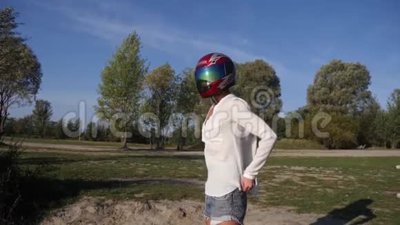 穿着摩托车头盔的快乐轻松的女孩在老村镇的池塘边视频的预览图