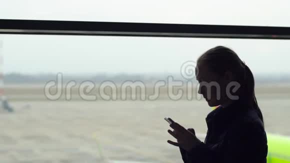 一名年轻女子在机场的一扇大窗户前用智能手机慢镜头视频的预览图
