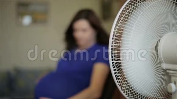 一个穿着蓝色连衣裙的孕妇正坐在一个白色扇子前面视频的预览图