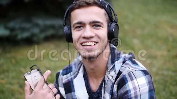 戴着耳机坐在草地上听音乐的男青年视频的预览图