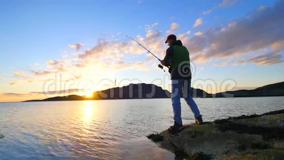 这个活跃的人正从岩石海岸在海上捕鱼渔民检查鱼线上的推饵准备好鱼竿并投掷视频的预览图