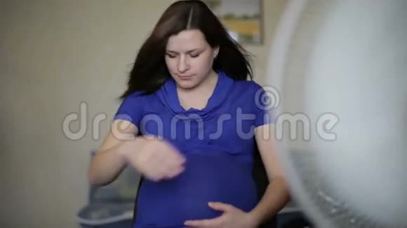 穿着蓝色连衣裙的孕妇坐在风扇前视频的预览图