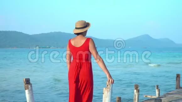 穿着红色长裙的女人这位穿红色衣服的年轻女子在码头上花钱远远地看着蓝色海洋视频的预览图