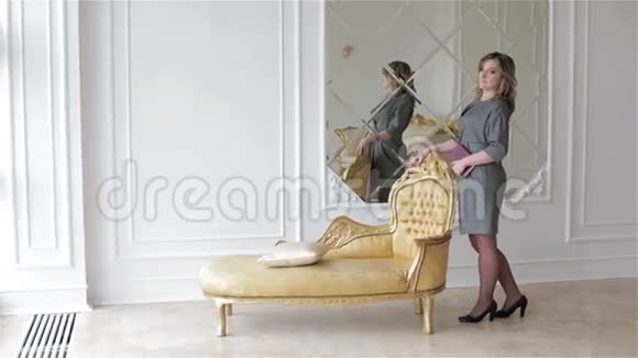 一位穿灰色连衣裙的年轻女子站在演播室的金色椅子附近视频的预览图
